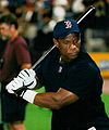 A dark-skinned man in a dark blue shirt. He is holding a black baseball bat over his shoulder in both hands. He is wearing a navy blue baseball cap with a red "B" outlined in white, and the same "B" logo is shown on his shirt at the neck.