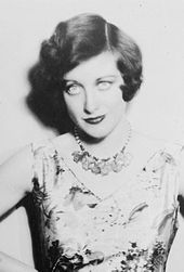 Upper body studio shot of a young Crawford in a sleeveless dress, with accented eye make-up, coiffed hair. She is staring into the camera.