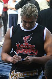 A male with blond hair wearing a black shirt signing an autograph.