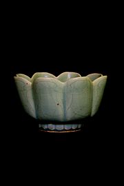 A blue-green bowl that assumes the form of several long ovals attached to each other on the longer sides, making the top rim of the bowl wavy.
