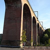 A large railway viaduct made from red bricks, topped by railings and electric pylons