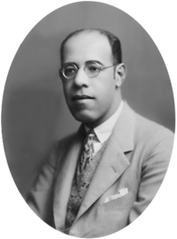 Photograph showing the head and shoulders of a man with glasses wearing a suit