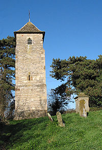 A plain tower with a pyramidal roof, a small lancet window, and a small louvred bell opening