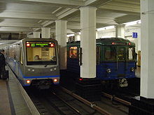 Two blue-and-gray trains—one new, one older—pulling into a station