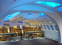 787 mock-up. It demonstrates the 787's spacious cabin. Above the brown seats are overhead bins.