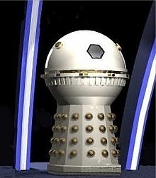 Full length image of a cream-coloured Dalek with a spherical head section and no appendages. The hemispheres and detailing around the dome mid-section are painted in gold.