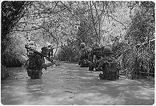 black & white photo Marines of Company H, 2nd Battalion, 4th Marine Regiment wading through a waist deep river in a jungle