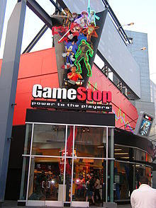 Ground view of a one-story building with windows running along the face of the building. The store name above its front entrance is accompanied by video game mascots and a gamer.