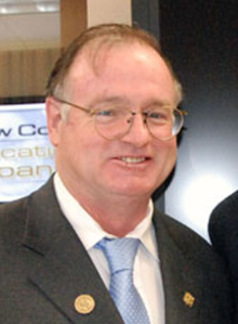 A white man with glasses wearing a suit and a tie
