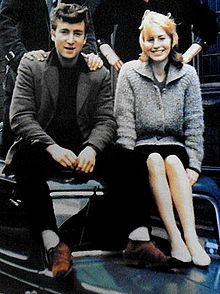 John on left, Cynthia on right, sitting side by side on the roof of a car.
