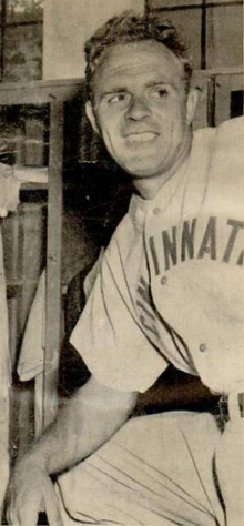 A man wearing a baseball uniform with "Cincinnati" written across the chest stands leaning on a propped up knee and smiles as he looks to the right.