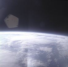 The edge of the Earth, heavily overexposed, in the lower half of the image, with black space above. In between them, a blue haze layer from the atmosphere. There is a lens flare in one corner.