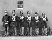 black & white photograph of six Marines standing in line, five with Civil War-era rifles and one with an NCO sword