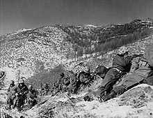 A line of soldiers on a hill under a boulder engaged in a battle
