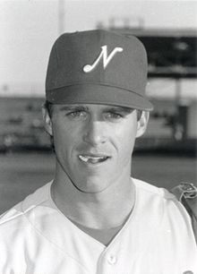 A black and white photograph of a man wearing a white baseball jersey and a cap with an "N" printed on it.