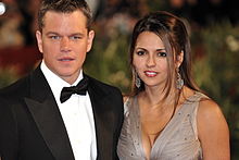 Damon in a tuxedo and bow-tie, with his wife wearing a low-cut, silver gown.