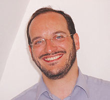 An Image of Rabbi Naftali Schiff.  Schiff is a middle-aged, balding man with a full beard, smiling at the camera.