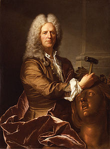 A portrait of sculptor Nicolas Coustou in full grey wig, his expression with a slight smile, and holding a hammer, with which he is working on the head of a large bronze female figure