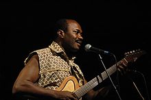 Upper body photograph of a Congolese man playing an electric guitar