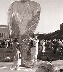 Piccard and Jeannette Piccard holding a plastic balloon in front of dozens of observers in what appears to be a stadium