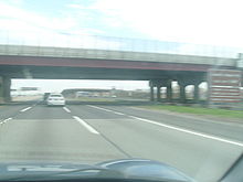 A large bridge hovering a 12-lane wide highway viewed from a car