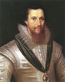 A portrait of Robert Devereux, who is portrayed wearing a silver shirt.  He has shoulder-length black hair and a brown beard which reaches down to his collar.  Devereux is wearing a medal suspended from a green ribbon.
