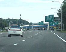 Ground-level view of four lanes of a busy freeway; several green exit signs and two overpass bridges are visible in the distance.