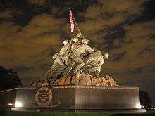 Color photo of the USMC War Memorial, a bronze statue of six men planting a flagpole with an American Flag into the ground.