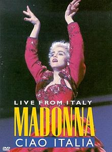 A blond woman in short cropped hair, wearing a red flamenco dress. She puts up both of her hands above her head. On top of her image, the word "Madonna" is written in yellow, with the words "Ciao Italia" written below in white, within a blue rectangualr box.