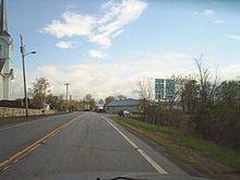 Ground-level view of a road with two green and white roadsigns. A church is visible on the left.