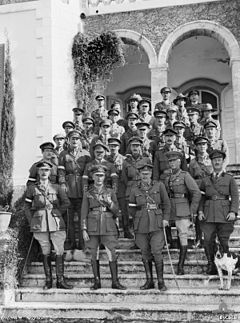 About thirty soldiers and two dogs pose on the steps of a building beneath a pair of arches