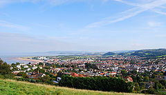Town seen from a nearby hill with multiple houses. The sea can be seen on the left and the white tent like canopy left of centre is the Butlins centre.