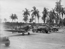 Single-engined military aircraft parked on tropical field beside petrol trucks