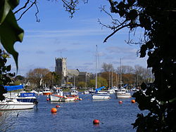 Looking across river with boats on we can see the priory against a bright blue sky