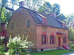 A small brick house with gambrel roof and red trim