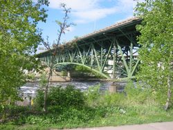 picture of the bridge painted green and surrounded by green foliage seen from the Mississppi bank