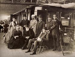 The Empress, Emperor and grandson sit on the promenade deck of an ocean liner, surrounded by their entourage.