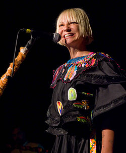 Upper body photo of a woman singing at a microphone.