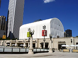 A large white tent sits on the roof of a cafe building set in front of a skyscraper and blue sky.