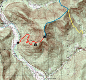 A topographic map with brown contour lines on a green and white background with red, blue and yellow routes overlaid along with black and white icons. Three roads alongside the edge of the map have signs with the numbers 28, 212 and 214.