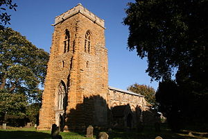 A tall church tower seen from the southwest with a battlemented parapet; the body of the church stretches beyond it