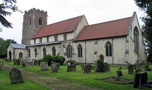 A stone church with red tiled roofs seen from the southeast, showing a battlemented tower, a nave with a clerestory, a south porch and a chancel