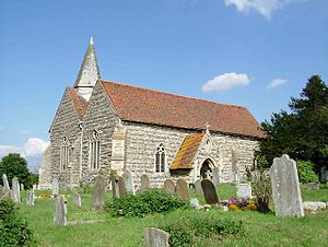 A stone church with red tiled roofs, showing the nave and aisle beside each other, a small spire, and the south porch