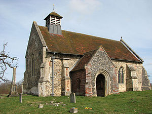 A small stone church with a red tiled roof seen from the southwest, showing a south porch and a small bellcote