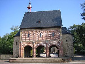 The 9th-century Torhalle (gatehouse) is a unique survival of the Carolingian era. It curiously combines some elements of the Roman triumphal arch (arch-shaped passageways, half-columns) with the vernacular Teutonic heritage (baseless triangles of the blind arcade, polychromatic masonry).