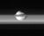 A bright fuzzy band (rings of Saturn) is running from the left to right. In the center a bright irregularity shaped body is superimposed on its upper edge. A narrow grayish band, which is a part of the main band, partially covers the body.