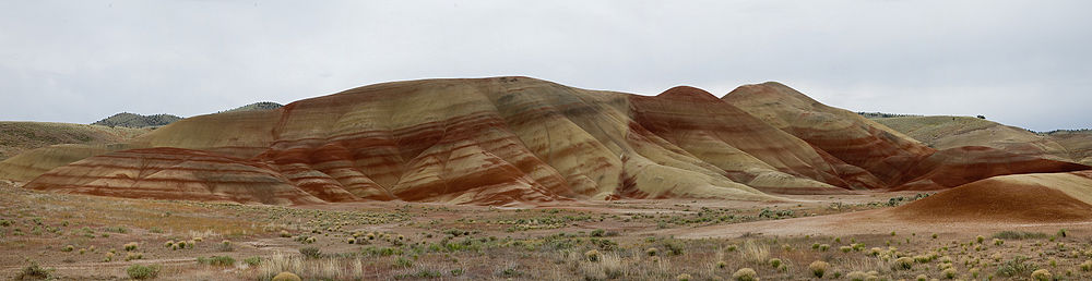 Multicolored rock strata in shades of red and yellow comprise a set of low, bare, rounded hills