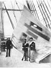 Large foreign flag behind three 1870s soldiers or sailors on a shipdeck
