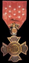 A bronze cross pattée, with the center of each arm extended in a semi-circular shape; in the center of the front is the word BREVET, encircled by the words UNITED STATES MARINE CORPS. A small five-pointed star, point-up, is at the bottom center of the circle formed by the inscription. A small Marine Corps insignia (eagle, globe and anchor) attaches the medal to its suspension ring.