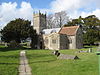 Stone building with square tower. Foreground is grass with gravestones.